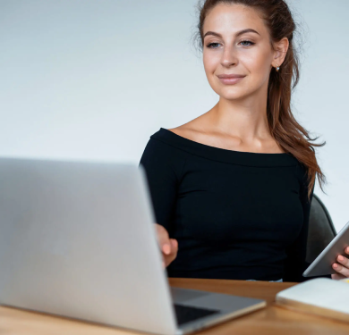 Smiling woman at a desk with laptop and tablet.