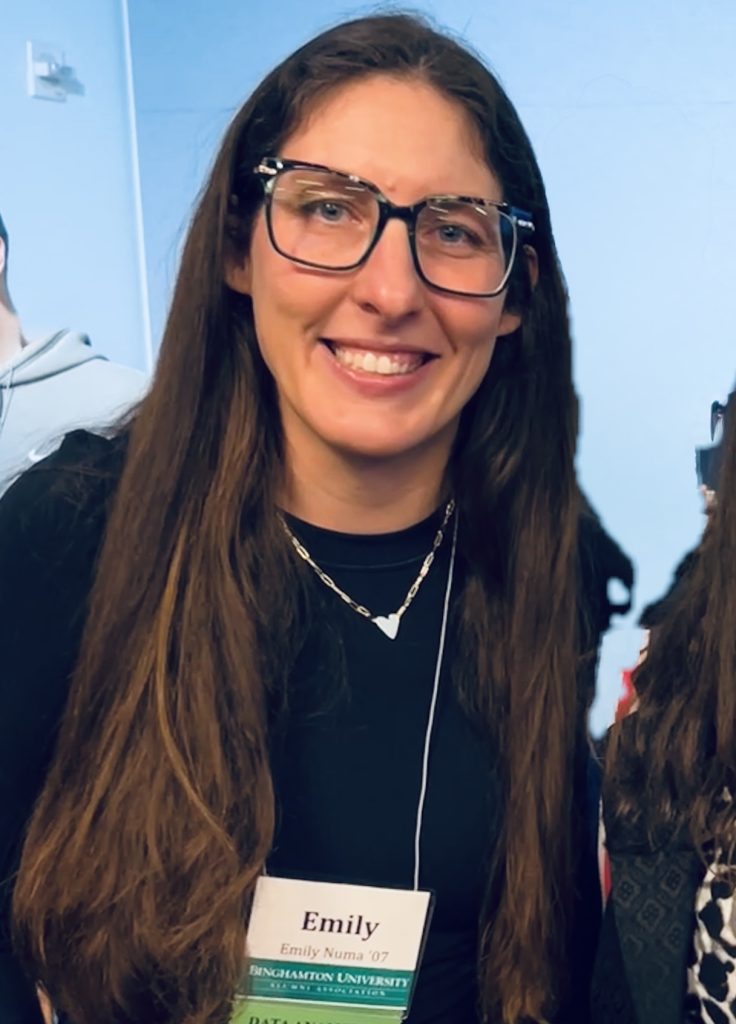 Tutor Emily smiling at the camera, wearing glasses and a black top, at a university alumni event.